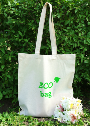 Natural Coloured Canvas Tote Bag With Eco Bag Branding, In a Natural Setting With Bushes/Trees Behind