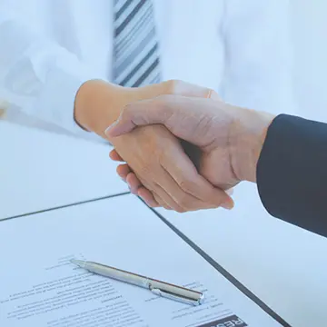 Close up of a handshake, with a signed document in the background.